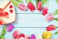 Colorful spring tulip flowers with decorative giftbox and hearts on light blue wooden background as greeting card with free space. Royalty Free Stock Photo