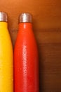 Colorful stainless thermo bottles, on a wooden table sprayed with water.