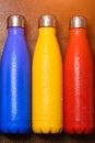 Colorful stainless thermo bottles, on a wooden table sprayed with water.