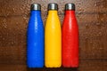 Colorful stainless thermos bottles on a wooden table sprayed with water.