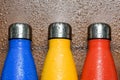 Colorful stainless thermos bottles on a wooden table sprayed with water.