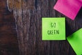 Colorful sticky notes on wooden background board reminder with copyspace. Go green written sticker on pineboard. Save the nature