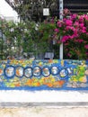 Colorful street mural of 9 muses on fence with pink flower Bush growing