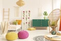 Colorful and stylish boho kid`s bedroom with peacock chair, single metal bed and green wooden cabinet