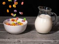 Colorful sugary cereals falling into a white bowl and milk jug in the background Royalty Free Stock Photo