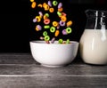 Colorful sugary cereals falling into a white bowl and milk jug in the background Royalty Free Stock Photo