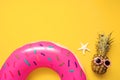 Colorful summer flat lay with pink inflatable circle donut, funny pineapple in sunglasses and starfish over yellow background