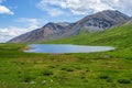 Colorful summer landscape with beautiful lake in sunlit green mountain valley among rocks and high mountain ridge under blue sky. Royalty Free Stock Photo