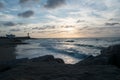 Colorful sunset in a calm ocean bay with a lighthouse and stones in the foreground. Royalty Free Stock Photo