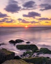 Colorful sunset glow and dramatic clouds over jetty rocks in the ocean