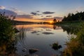 Colorful sunset over a calm lake with reflections in the water and rocks and reeds in the foreground Royalty Free Stock Photo