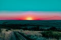 A colorful sunset over a clear sky of unusual color, around uneven large and spacious fields with green vegetation