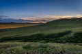 Colorful sunset over green hills with sheep in the middle and the outline of a temple on the ridgeline in Inner Mongolia