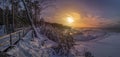 Colorful sunset over snowy sea coast and pine forest with wooden boardwalk path. Beautiful view of Baltic sea coast with snow- Royalty Free Stock Photo