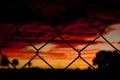 Colorful sunset with palms behind a mesh fence symbol for poor and rich and contrast