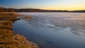 Colorful sunset on the shore of a lake in early spring. Reeds and trees in the distance. The surface half-covered with ice