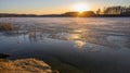 Colorful sunset with sun beams on the shore of a lake in early spring. Reeds and trees in the distance. The surface half-covered