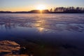 Colorful sunset with sun beams on the shore of a lake in early spring. Reeds and trees in the distance. The surface half-covered