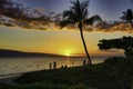 Colorful sunset view of Lanai from Maui with silhouetted people near shore.