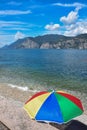 Colorful sunshade at garda lake shore, sailboat on the lake and mountains behind