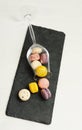 Colorful french mini macarons sprinkled from an overturned wine glass on slate board. White background