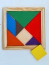 Colorful tangram puzzle in wooden frame on white wood background.