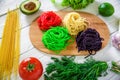 Colorful tasty pasta on board and raw vegetables on rustic table. Flat lay. Top view