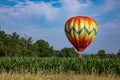 Colorful Teardrop Shaped Hot Air Balloon Over Corn Field on Sunny Day with Trees and Cloudy Blue Sky Royalty Free Stock Photo