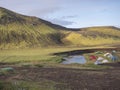 Colorful tents at camping site on blue Alftavatn lake with green hills and glacier in the otherwordly beautiful