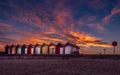 Colorful vibrant beach huts and promenade on the seafront with beautiful cloudy sunset behind. Royalty Free Stock Photo