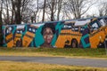 A colorful wall mural of an African American woman and a yellow school buss surrounded by yellow winter grass