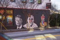 a colorful wall mural with Colin Kaepernick kneeling, Jimmy Carter, and a clown on a black brick wall in Atlanta Georgia