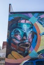 A colorful wall mural of people on the side of a brick building in Little Five Points surrounded by parked cars