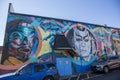 A colorful wall mural of people on the side of a brick building in Little Five Points surrounded by parked cars