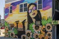 A colorful wall mural with a woman wearing sunglass, surfers at the beach and colorful flowers on the side of a building