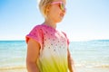 Smiling trendy girl in colorful shirt on seashore looking aside