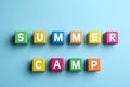 Colorful cubes with phrase SUMMER CAMP on light blue background, flat lay