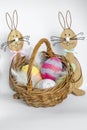 Colorful wooden easter bunnies with a wicker basket filled with knitted easter eggs Royalty Free Stock Photo