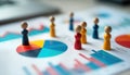 Colorful wooden figures stand on document with charts, graphs. Pie charts, bar graphs display data. Figures represent different