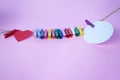 Colorful wooden paper clips with red heart and blank white circle paper for text note message attached on pink background.