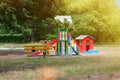 Colorful wooden playground on yard in park. Girl is resting on children playground surrounded by green trees in sunlight morning Royalty Free Stock Photo