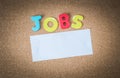 Colorful Wooden word JOBS with piece of White paper on cork board