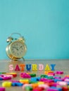 Colorful wooden word SATURDAY on wooden table and vintage alarm clock and background is powder blue. English alphabet made of wood Royalty Free Stock Photo