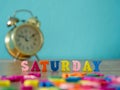 Colorful wooden word SATURDAY on wooden table and vintage alarm clock and background is powder blue. English alphabet made of wood Royalty Free Stock Photo