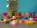 Colorful wooden word WEDNESDAY on wooden table and vintage alarm clock and background is powder blue. English alphabet made of woo