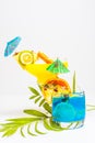 Colorful yellow and blue summer cocktails decorated with tropical fruits, umbrellas and straws on white background with palm tree Royalty Free Stock Photo