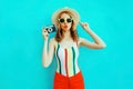 Colorful young woman holding retro camera, blowing red lips sends air kiss in summer straw hat having fun on blue wall Royalty Free Stock Photo