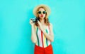 Colorful young woman holding retro camera, blowing red lips sends air kiss in summer straw hat having fun on blue wall Royalty Free Stock Photo
