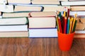 Colorfull pencils in plastic holder and stack of old book on wooden table, education concept background, many books piles with