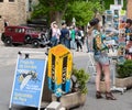 Colorfully dressed woman browses postcard display on street with vintage Kodak sign